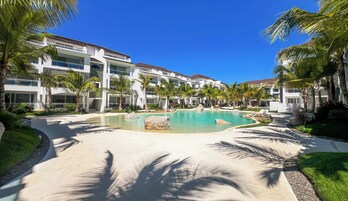 Un resort con piscina central, palmeras y edificios modernos.