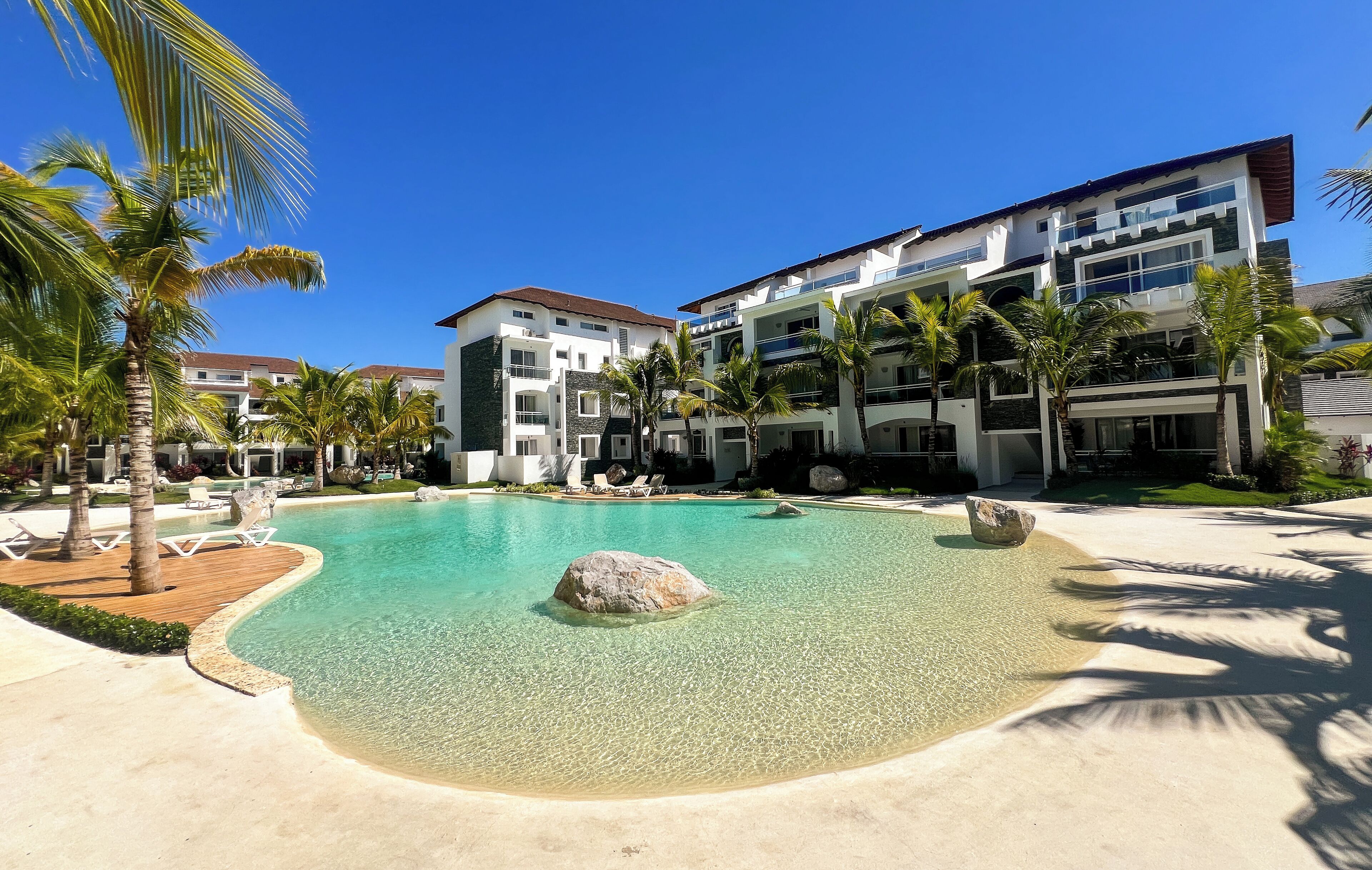 A resort with a clear pool, palm trees, and modern buildings.