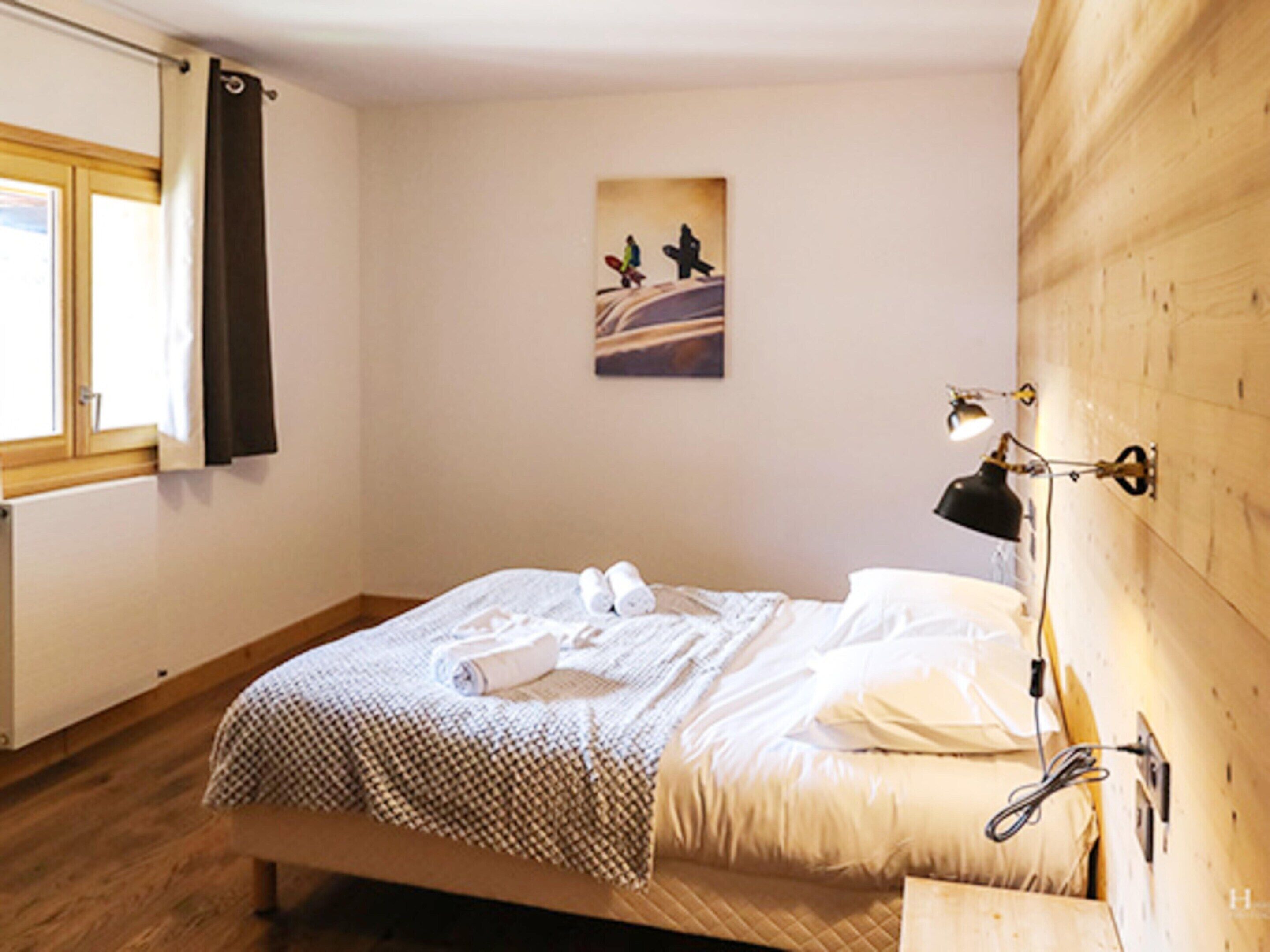 A bedroom with a wooden bed, a bedside lamp, and a window with curtains.