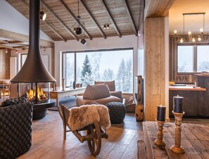 A cozy living room with a fireplace, wooden furniture, and a large window with a snowy view.