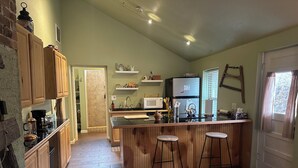 Una cocina con armarios de madera, una isla central con taburetes, un refrigerador y un microondas.