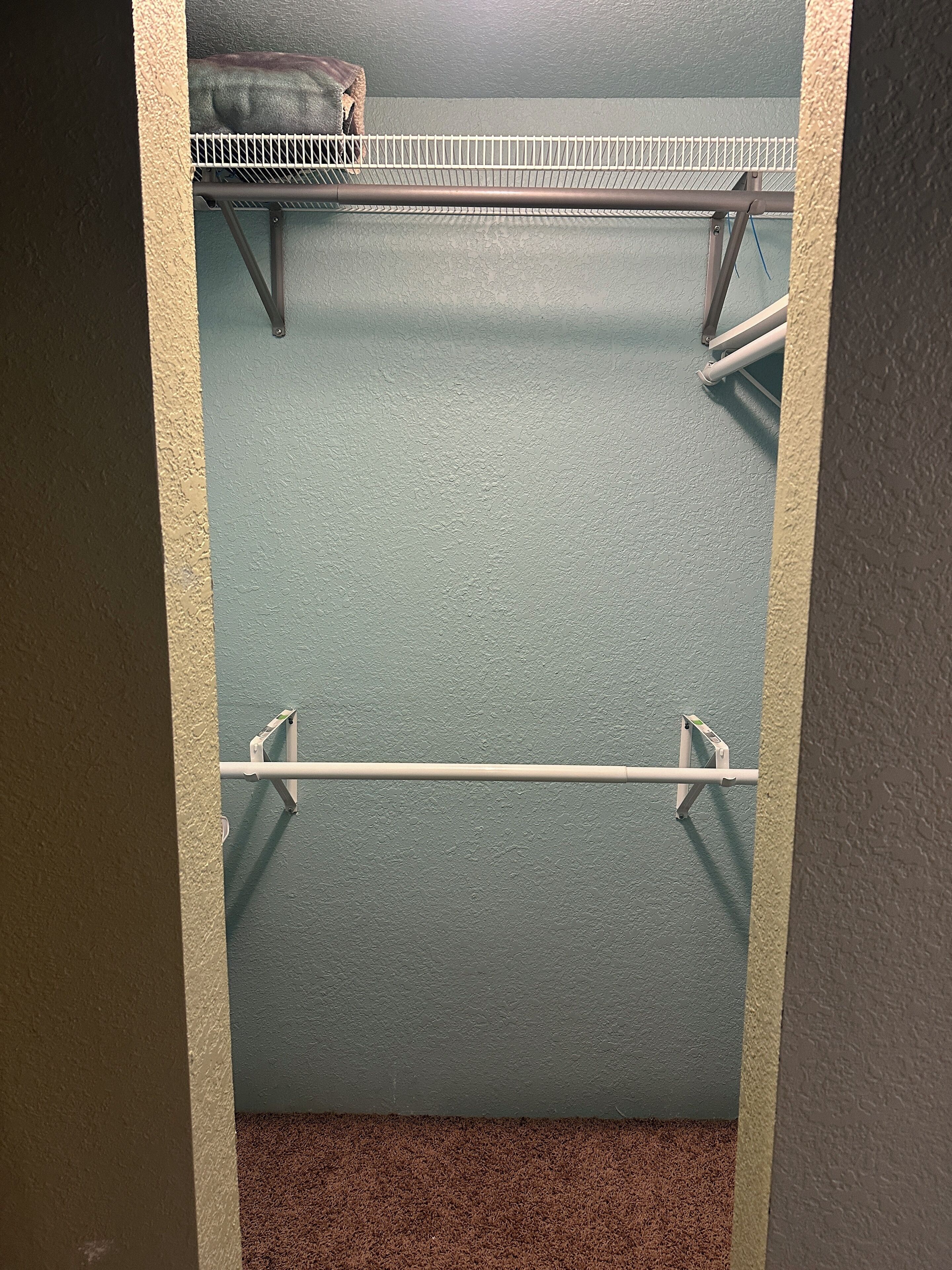 Ein Schrank mit Metallstange und Kleiderstange, eine blau strukturierte Wand und ein brauner Teppichboden.
