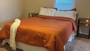 Un dormitorio con cama, mesita de noche, ventana con persianas y suelo cubierto de alfombra.