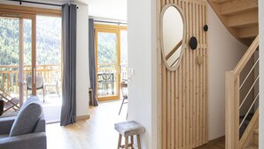 A spacious living area with a wooden staircase, a large window with a view of the outdoors, and a modern design with a wooden accent wall and a round mirror. - Apartment in Vaujany Near Alpe D'huez Ski Area (Vaujany)