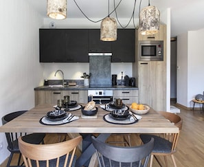 A modern kitchen with dark cabinets, a wooden dining table, and pendant lights. - Apartment in Vaujany Near Alpe D'huez Ski Area (Vaujany)
