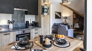 A modern kitchen with dark cabinets, a microwave, and a dining area with a wooden table set for a meal. - Apartment in Vaujany Near Alpe D'huez Ski Area (Vaujany)