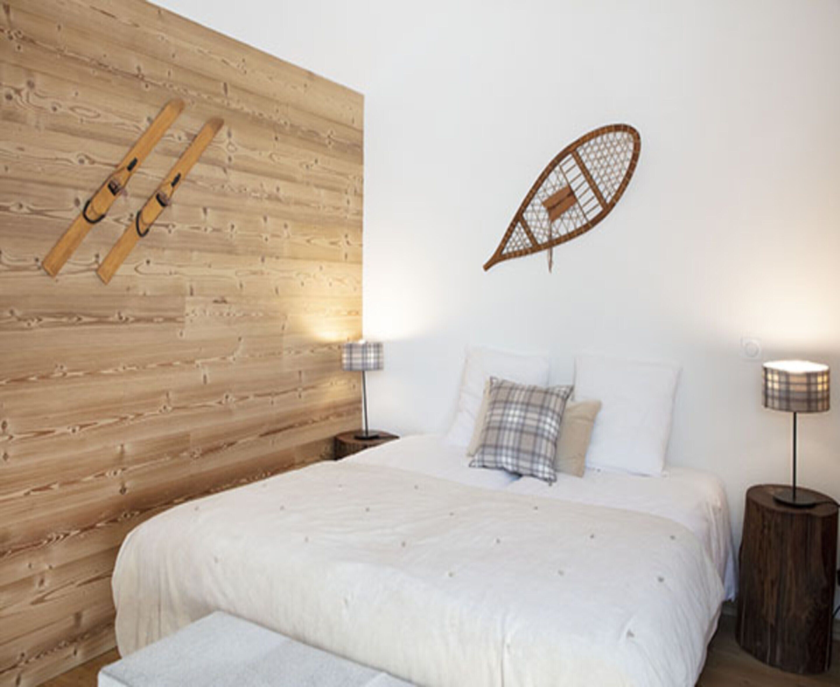 A bedroom with a wooden headboard, a bed with white bedding, two bedside tables with lamps, and a wall-mounted shelf.