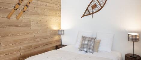 A bedroom with a wooden headboard, a bed with white bedding, two bedside tables with lamps, and a wall-mounted shelf.