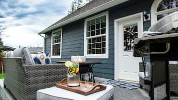 An outdoor seating area with a wicker sofa, a tray with a pitcher of iced tea, and a grill.