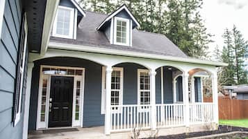A two-story house with a front porch, a black front door, and a small garden area.