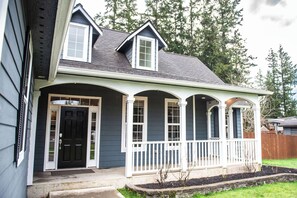 A two-story house with a front porch, a black front door, and a small garden area. - Magnolia Suites, A Coastal Retreat, 4 Bed 2 Bath (Forks)