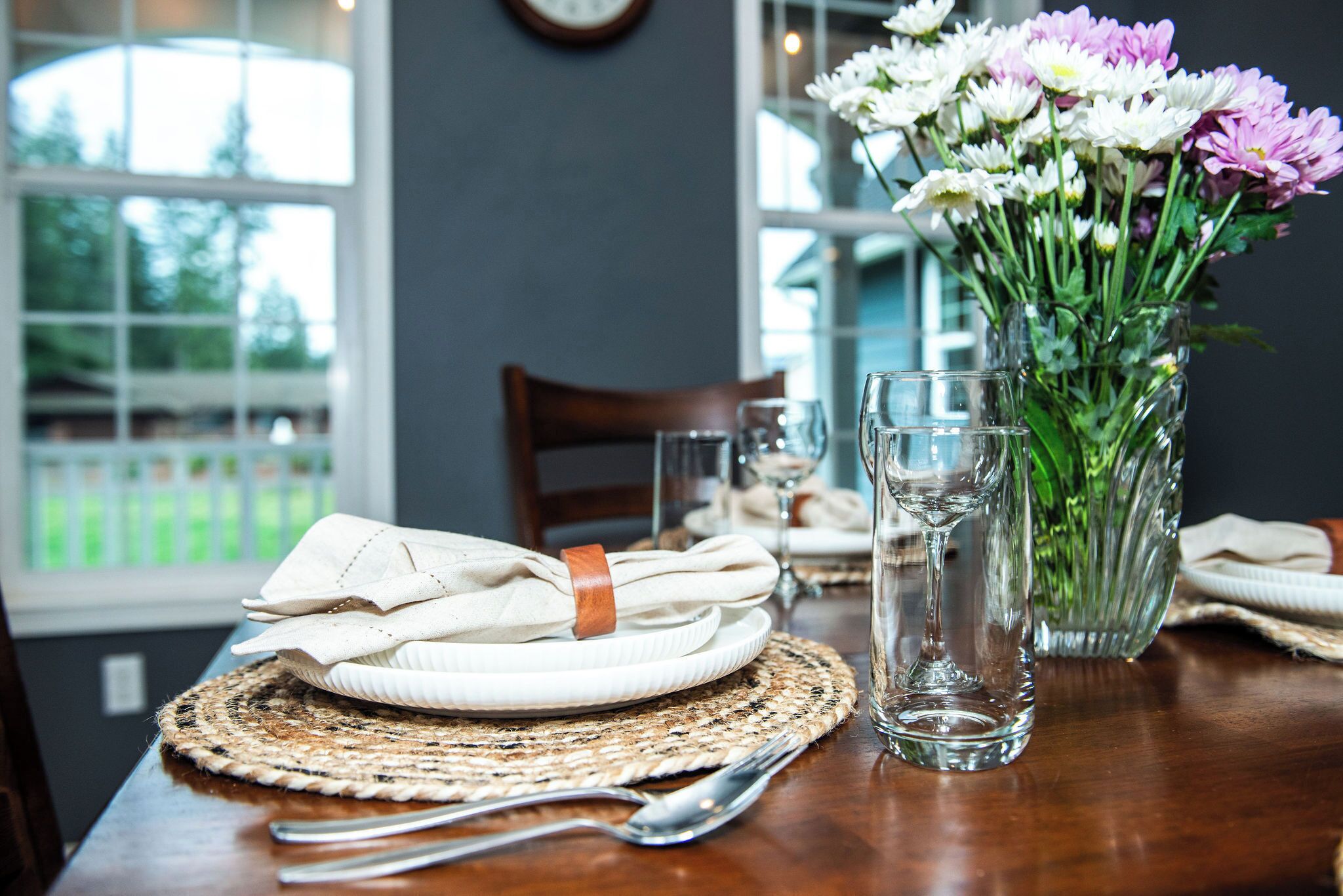 Una mesa de comedor con un mantel tejido, un florero de vidrio transparente y una servilleta doblada con una banda de cuero.