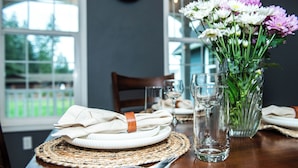 Una mesa de comedor con un mantel tejido, un florero de vidrio transparente y una servilleta doblada con una banda de cuero.