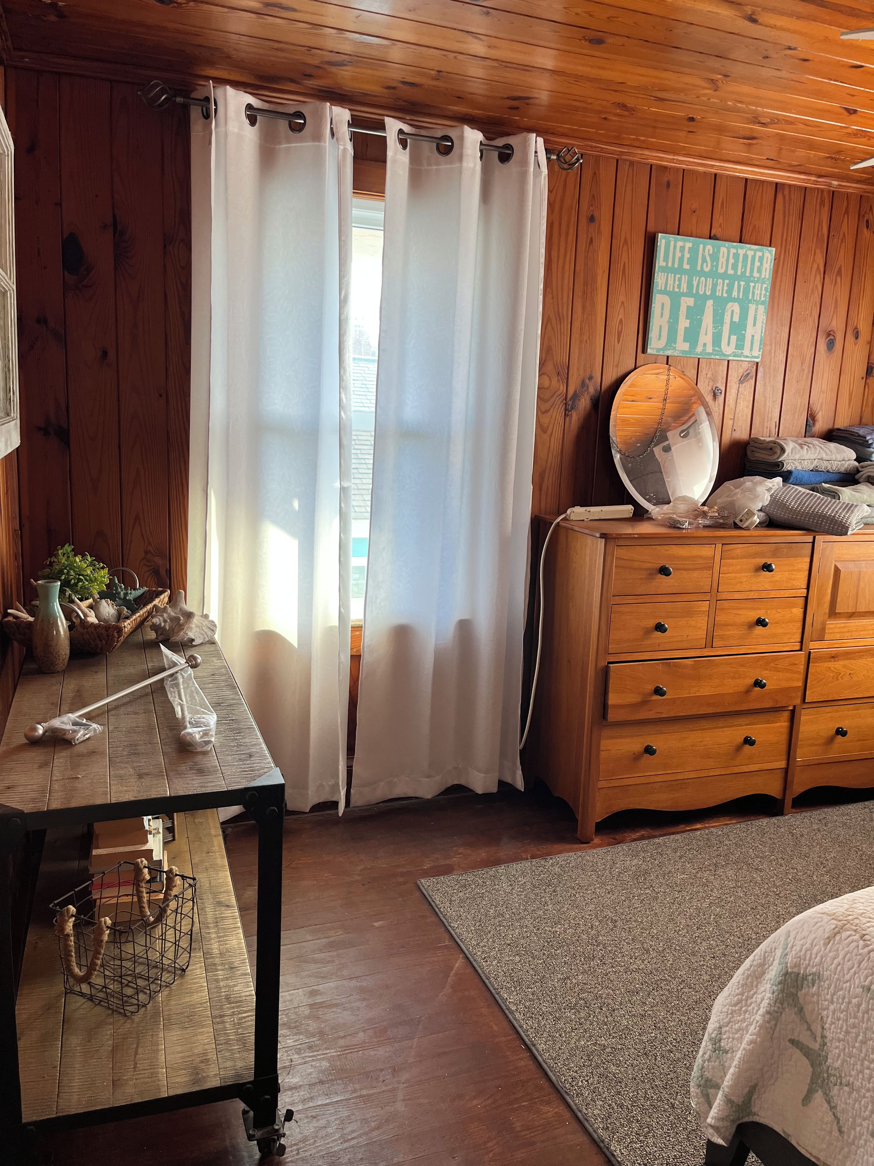 Une pièce aux murs en bois, une commode en bois avec des tiroirs, un miroir et un panneau accroché au mur.