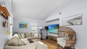 A living room with a sectional sofa, a wicker chair, a flat-screen TV, and artwork on the walls.
