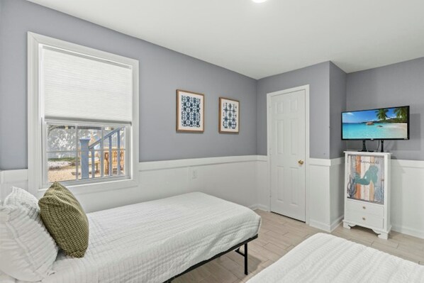 A bedroom with two beds, a television, and artwork on the wall.