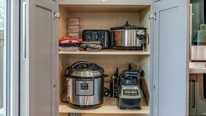 A kitchen cabinet with shelves holding plates, cookware, and a coffee maker.