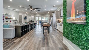 A modern kitchen with a central island, a dining area with a pool table, and a living room with a gray sofa and a TV.