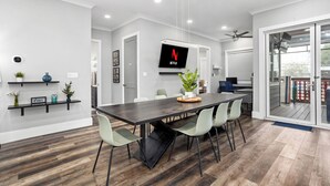 A modern dining area with a long table, light green chairs, and a mounted TV displaying the Netflix logo.