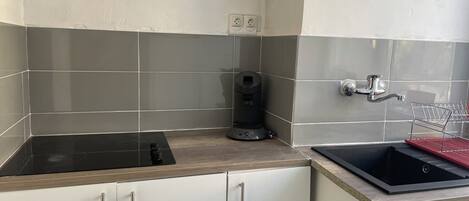A kitchen with a black stove, a coffee machine, a sink, and a dish rack.