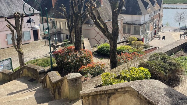 A riverside view with buildings, a bridge, and a staircase leading down. - Le Gambetta (Gien)