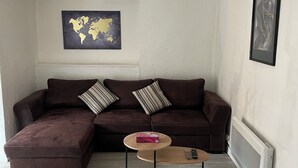A living room with a brown sectional sofa, a round wooden coffee table, a world map on the wall, and a radiator. - Le Gambetta (Gien)
