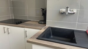 A kitchen with white cabinets, a black sink, and a stove. - Le Gambetta (Gien)