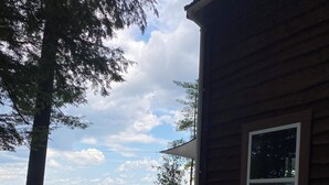 Eine Holzhütte mit einer Veranda, einem großen Fenster und Blick auf ein Gewässer und Berge.