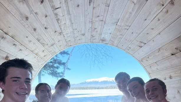 Eine Gruppe von Personen sitzt in einer Holzhütte mit Blick auf eine verschneite Landschaft.
