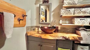 Ein kleines Badezimmer mit einem Holzwaschtisch, einem Kupferbecken und Aufbewahrungsboxen.