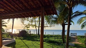 Un espacio al aire libre techado con vista al mar, palmeras y un sendero que lleva a una puerta.