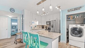 A modern kitchen with white cabinets, a central island, and a washing machine. - Oceanfront Complex | Heated Pool/Tennis | Grnd FL (Cocoa Beach)