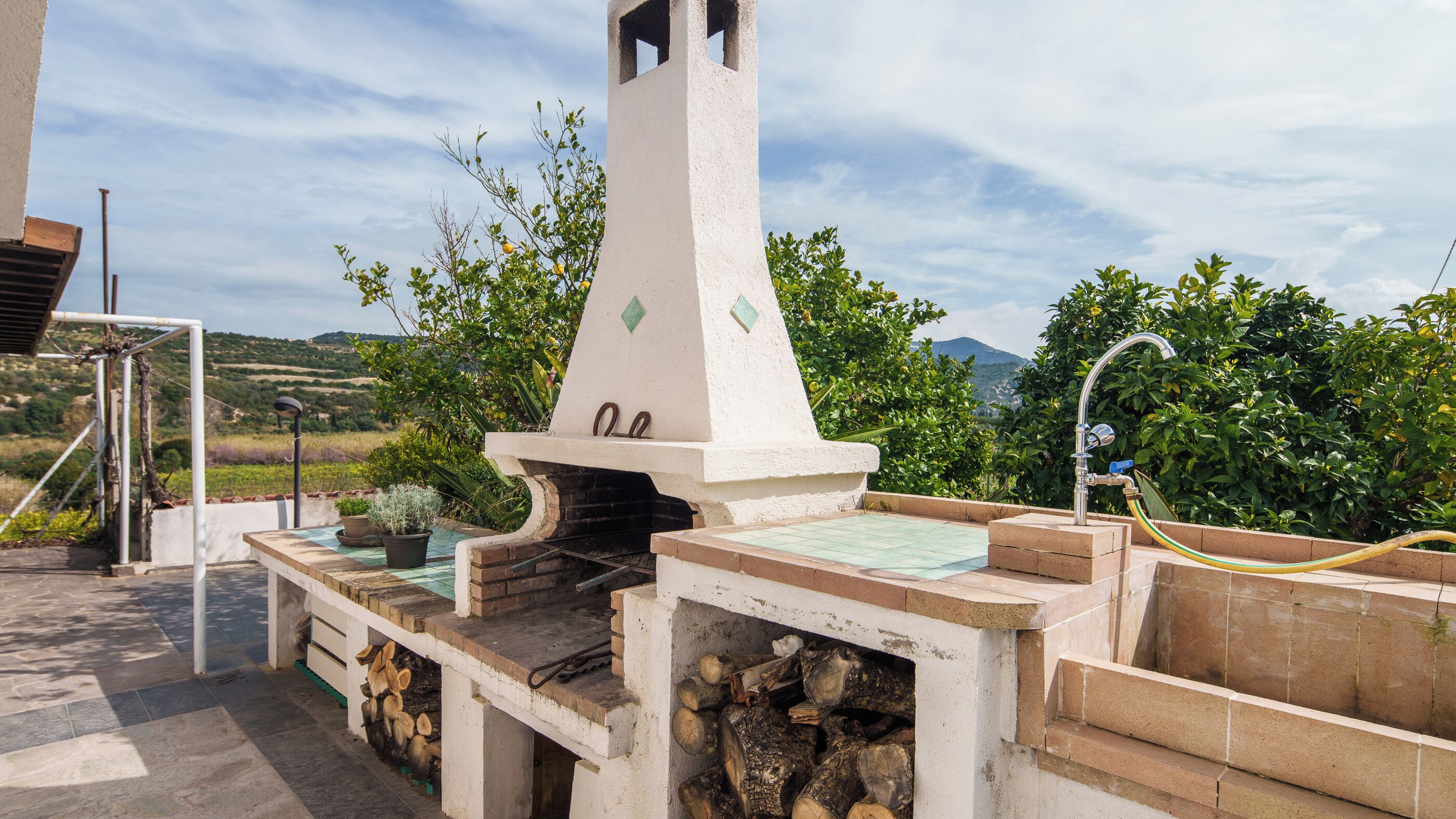 Un espace barbecue équipé d’une cheminée, d’une table carrelée et d’un tuyau d’arrosage.