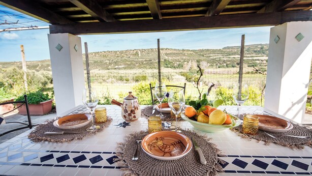 An outdoor dining area with a view of the countryside, featuring a table set with plates, glasses, and a fruit bowl. - La Villa del Relax - Two Bedroom Villa, Sleeps 4 (Sennori)
