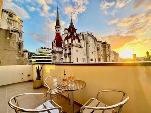 Une terrasse avec une table et des chaises, d’où l’on peut admirer un bâtiment historique doté de deux flèches.