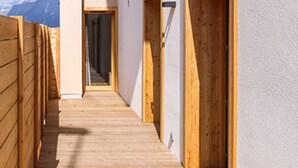 Un couloir étroit en bois, avec des portes en bois, d’où l’on aperçoit une montagne au loin.