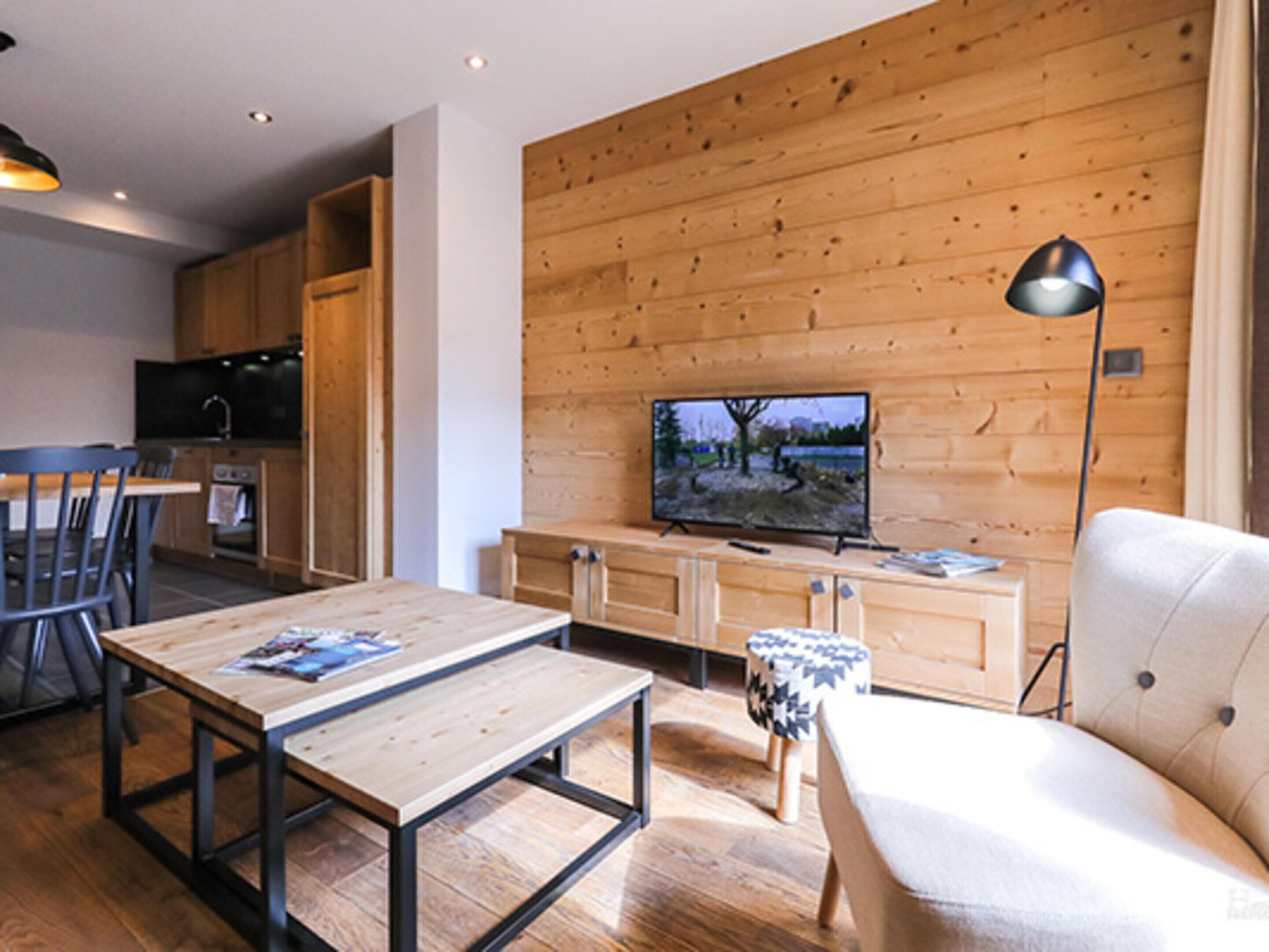 A modern living room with a wooden wall, a TV, a sofa, and a dining table.