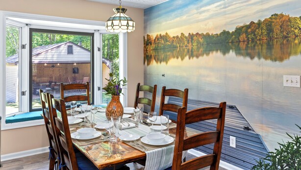 Un coin repas avec une table dressée pour quatre personnes, un vase rempli de fleurs et une fresque représentant un lac.