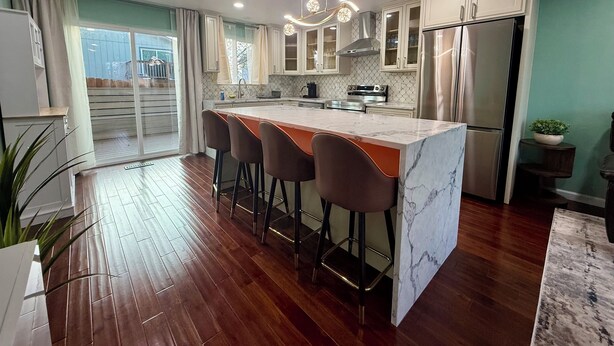 A modern kitchen with a marble island, stainless steel appliances, and a sliding glass door to a balcony.
