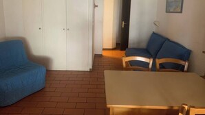 A room with a blue sofa, a wooden chair, a dining table, and a white wardrobe. - 180° sea view, direct beach access, close to town center (Bandol)