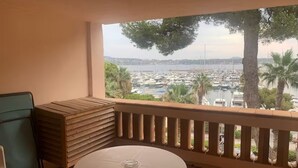 A balcony with a round table and chairs, overlooking a marina with boats and a distant cityscape. - 180° sea view, direct beach access, close to town center (Bandol)