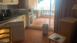 A compact kitchen with a sink, a coffee maker, and a small refrigerator. There is a dining area with a table and chairs, and a view of a balcony with a railing. - 180° sea view, direct beach access, close to town center (Bandol)