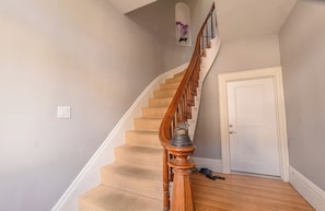 Una escalera con barandilla de madera y peldaños alfombrados en color beige que conducen a una puerta blanca.