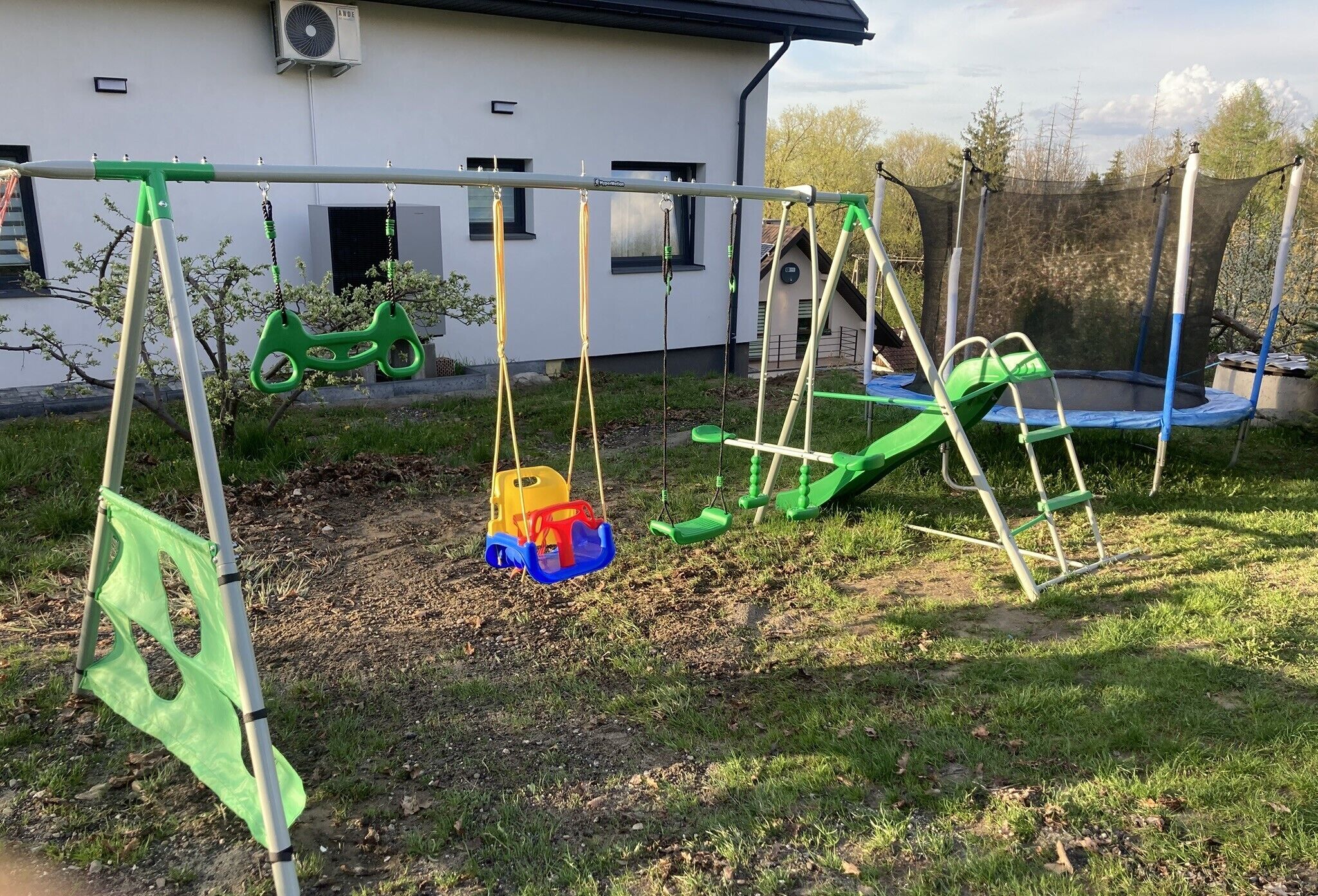 Een speeltuin met schommels en een trampolaan voor een wit gebouw.