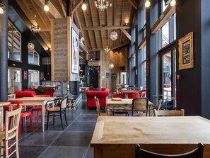 Een restaurantinterieur met houten balken, rode zitplaatsen en grote ramen.