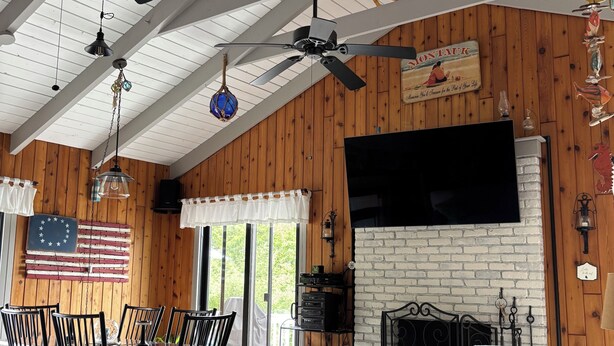 A spacious living room with a high ceiling, wooden walls, a fireplace, and a dining area with a table and chairs.