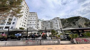 A modern hotel with multiple floors, outdoor seating, and a view of a rocky hillside. - Vista Adriatic CZ (Durres)