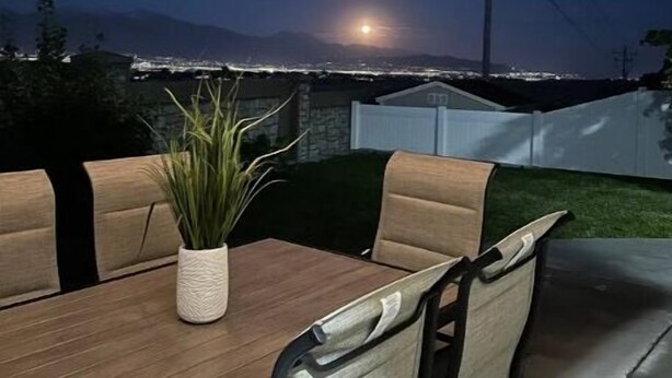 An outdoor patio with a table and chairs, a potted plant, and a view of the moon and mountains in the background. - Wake up to the best panoramic views in this cozy 3-bedroom house. (West Jordan)