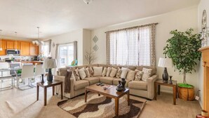 A living room with a sofa, coffee table, and a rug. There is a plant and a lamp on a side table. - Wake up to the best panoramic views in this cozy 3-bedroom house. (West Jordan)