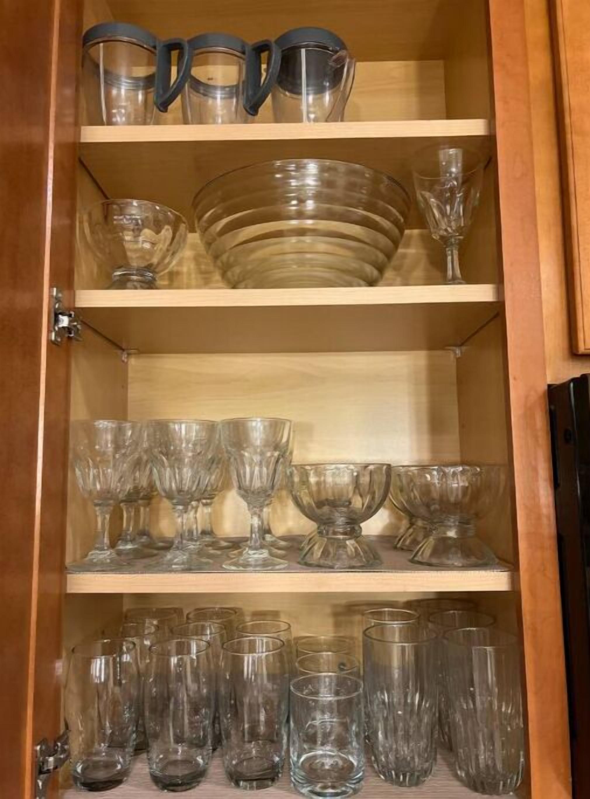 Een houten kast met planken vol verschillende glazen, zoals bekers, kommen en glaasjes.
